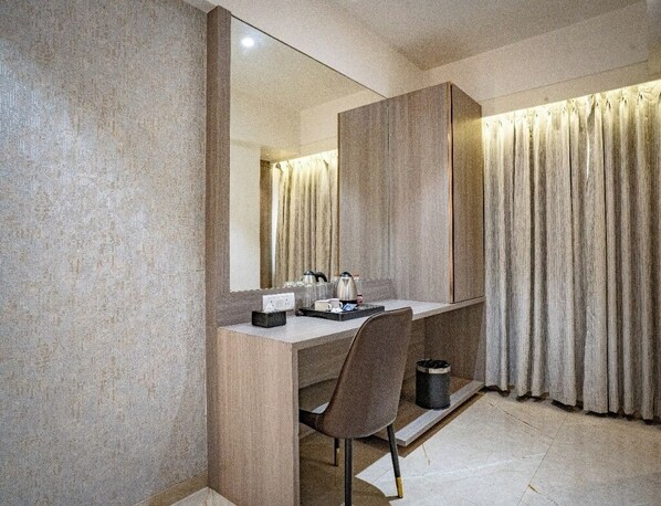 A modern hotel room with a large mirror, a wooden desk, a chair, and a trash bin.