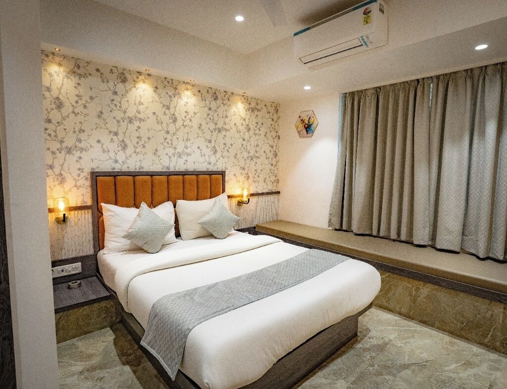 A bedroom with a bed, bedside lamps, a window with curtains, and an air conditioning unit.