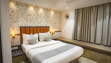 A bedroom with a bed, bedside lamps, a window with curtains, and an air conditioning unit.