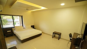 A bedroom with a bed, bedside tables, a small table, a desk, and a chair. - HOTEL VARAY EXPRESS (Ujjain)