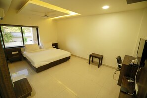 A bedroom with a bed, bedside tables, a small table, a desk, and a chair. - HOTEL VARAY EXPRESS  (Ujjain)