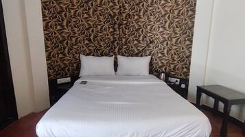 Ein Bett mit weißer Matratze und Kissen, ein dunkles Holz-Kopfbrett und eine gemusterte Wand dahinter.