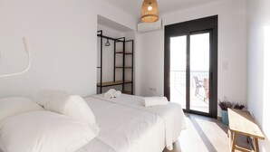 Un dormitorio moderno con una cama grande, una lámpara colgante, un balcón con vistas y una pequeña mesa de madera.