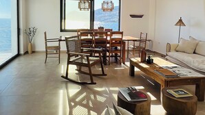 Un salón comedor amplio con un gran ventanal, un área de comedor con muebles de madera y una zona de estar acogedora con un sofá y una lámpara.