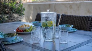 Ein Tisch im Freien mit einer großen Wasserflasche, mehreren Gläsern und Schalen mit Obst.