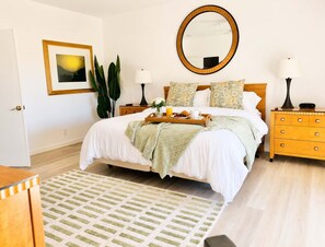 A neatly arranged bedroom with a bed, bedside tables, a mirror, and a framed picture on the wall.
