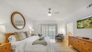 Ein Schlafzimmer mit Bett, Kommode, Spiegel, Deckenventilator und Fernseher an der Wand.