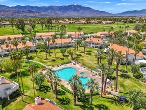 A resort with multiple buildings, a central swimming pool, and a mountainous backdrop.