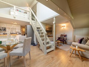 A spacious loft with a high ceiling, a staircase, a dining area with a glass table, and a cozy seating area with a sofa and armchairs.