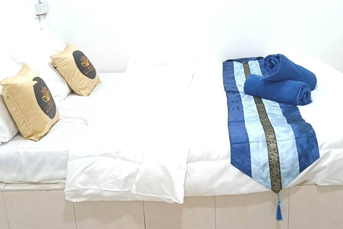 A bed with white bedding, two beige pillows with a logo, and a blue blanket with stripes.