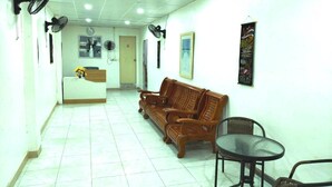 A reception area with a reception desk, wooden sofa, and two chairs. - Marine Guest House Encore (Pattaya)