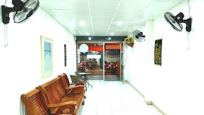 A hallway with wooden benches, ceiling fans, and a restaurant entrance. - Marine Guest House Encore (Pattaya)