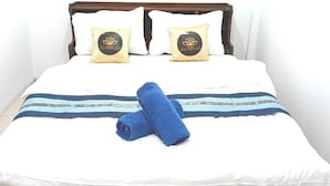 A neatly made bed with white bedding, two decorative pillows, and a blue towel. - Marine Guest House Encore (Pattaya)