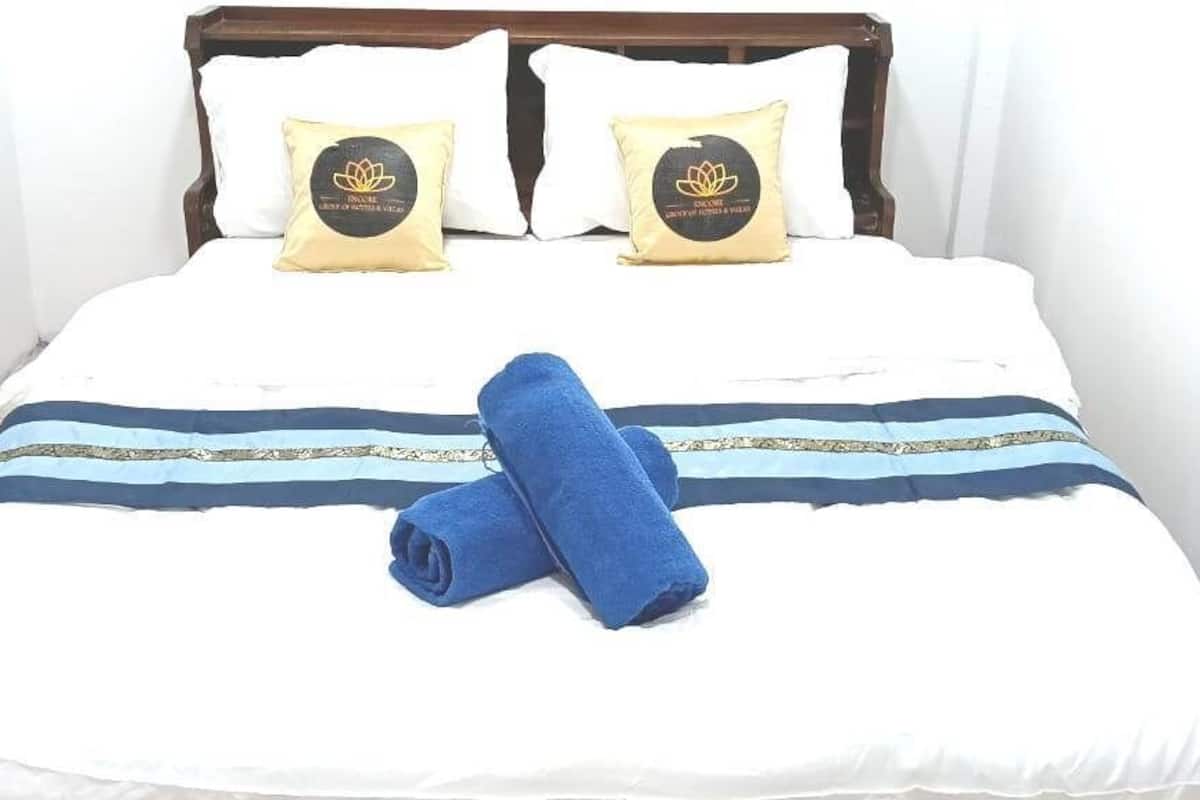A neatly made bed with white bedding, two decorative pillows, and a blue towel.