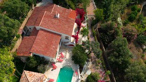 Vue aérienne d’une maison avec un toit en tuiles, une piscine et des chaises longues rouges.