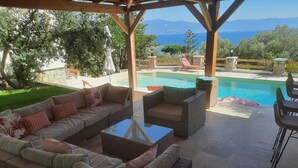 Un espace extérieur aménagé, abrité et doté de mobilier en osier, avec une piscine et une vue sur la mer.