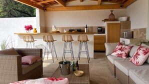Un espace extérieur accueillant, aménagé avec des meubles en osier, un bar avec des tabourets et une cuisine en arrière-plan.