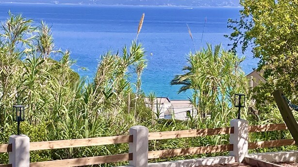 Une terrasse avec des sièges extérieurs, une vue sur la mer et une clôture en bois.