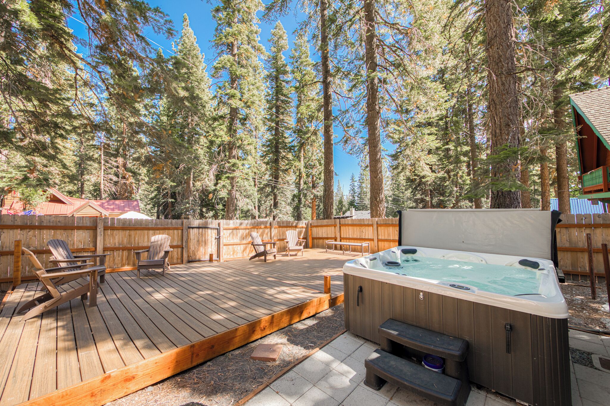 Una terraza de madera con jacuzzi, sillas y un cerco de madera en un área boscosa.
