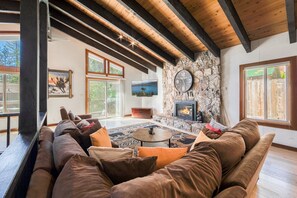 Un salón acogedor con chimenea de piedra, un sofá marrón grande y techo de madera.