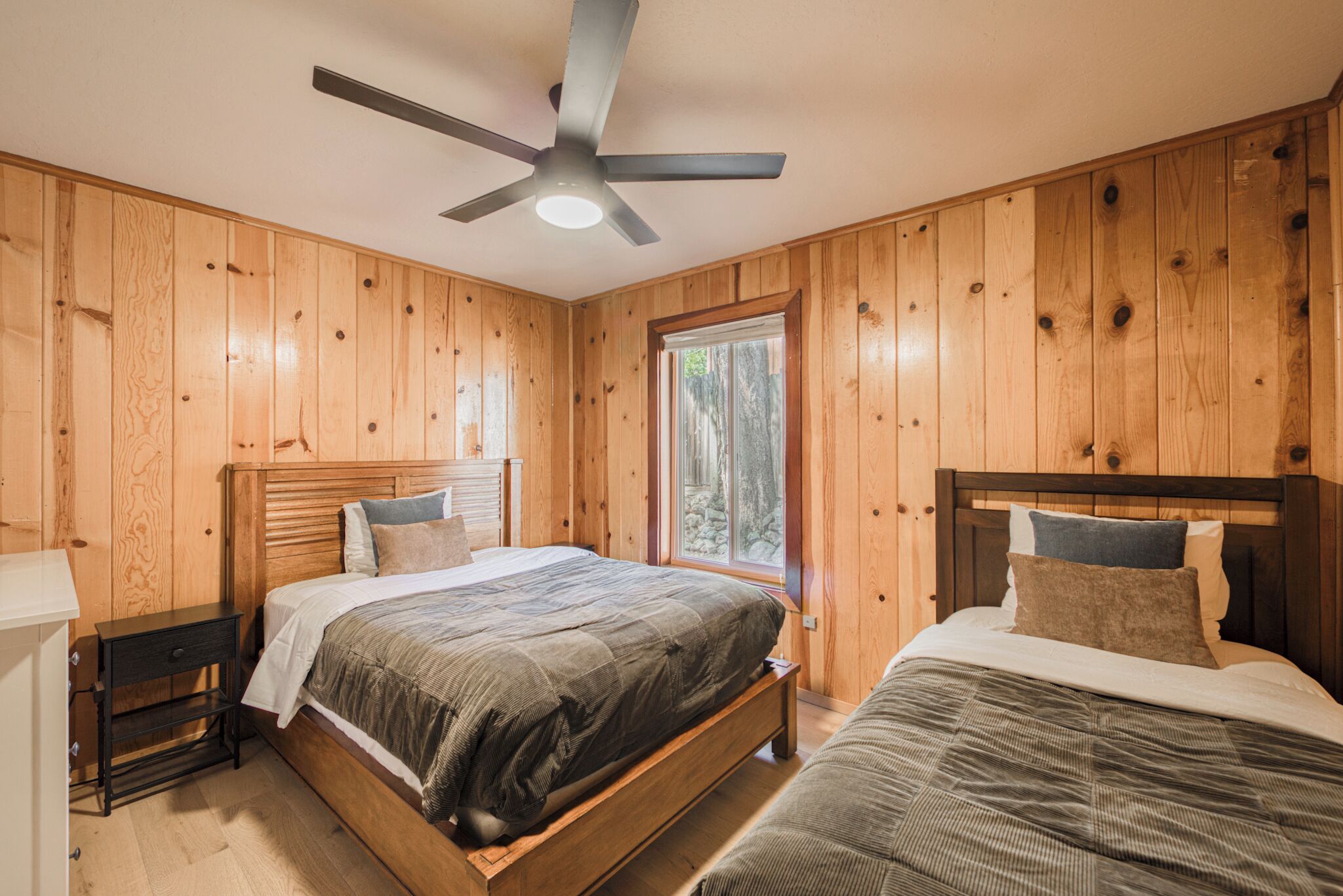 Ein Schlafzimmer mit zwei Betten, Holzwänden, einem Deckenventilator und einem Fenster.
