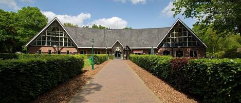 Stately building with a central entrance and two wings, set amidst beautifully manicured hedges.