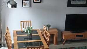 A dining area with a wooden table and chairs, a small plant, and a TV on a wooden stand. - Bangor - 2 Bed Apartment- Sleeps 4 -privateparking (Bangor)