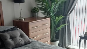 A bedroom with a patterned bedspread, a dresser, a lamp, and a potted plant. - Bangor - 2 Bed Apartment- Sleeps 4 -privateparking (Bangor)