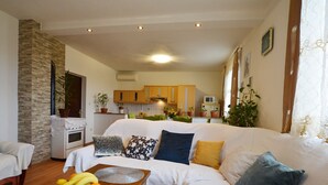Een gezellige woonkamer met een bank, een eettafel met fruit, en een keuken op de achtergrond.