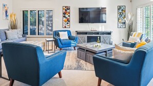 Un salon moderne avec un canapé bleu, un fauteuil bleu et une table basse. Un téléviseur à écran plat est fixé au mur, et une cheminée se trouve en dessous.