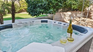 Un bain à remous avec une bouteille de vin et des verres, entouré d’un jardin agrémenté de palmiers et d’une balançoire.