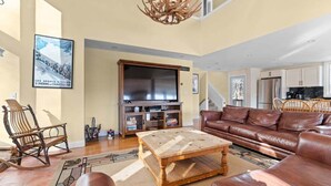 A spacious living room with a large flat-screen TV, leather sofas, a wooden coffee table, and a unique chandelier. - The Navillus House: Hot Tub, Ski On/Ski Off, A/C. Discounted Ski Rentals. (Killington)