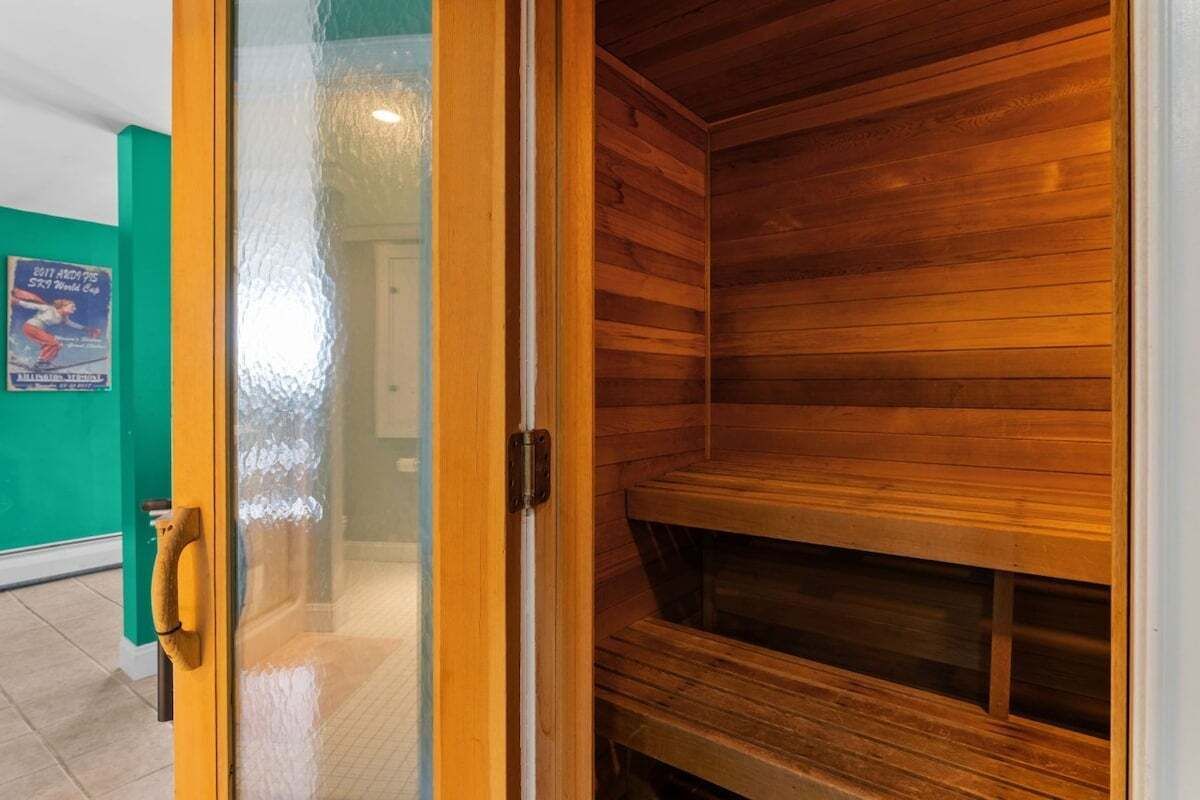 A wooden sauna with a glass door, a wooden bench inside, and a green wall in the background.