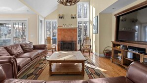 A spacious living room with a fireplace, leather sofa, wooden coffee table, and a large flat-screen TV. - The Navillus House: Hot Tub, Ski On/Ski Off, A/C. Discounted Ski Rentals. (Killington)