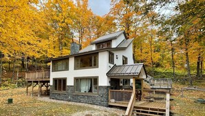 A two-story house with a stone foundation, a wooden deck, and a stone staircase leading to a porch. - The Navillus House: Hot Tub, Ski On/Ski Off, A/C. Discounted Ski Rentals. (Killington)