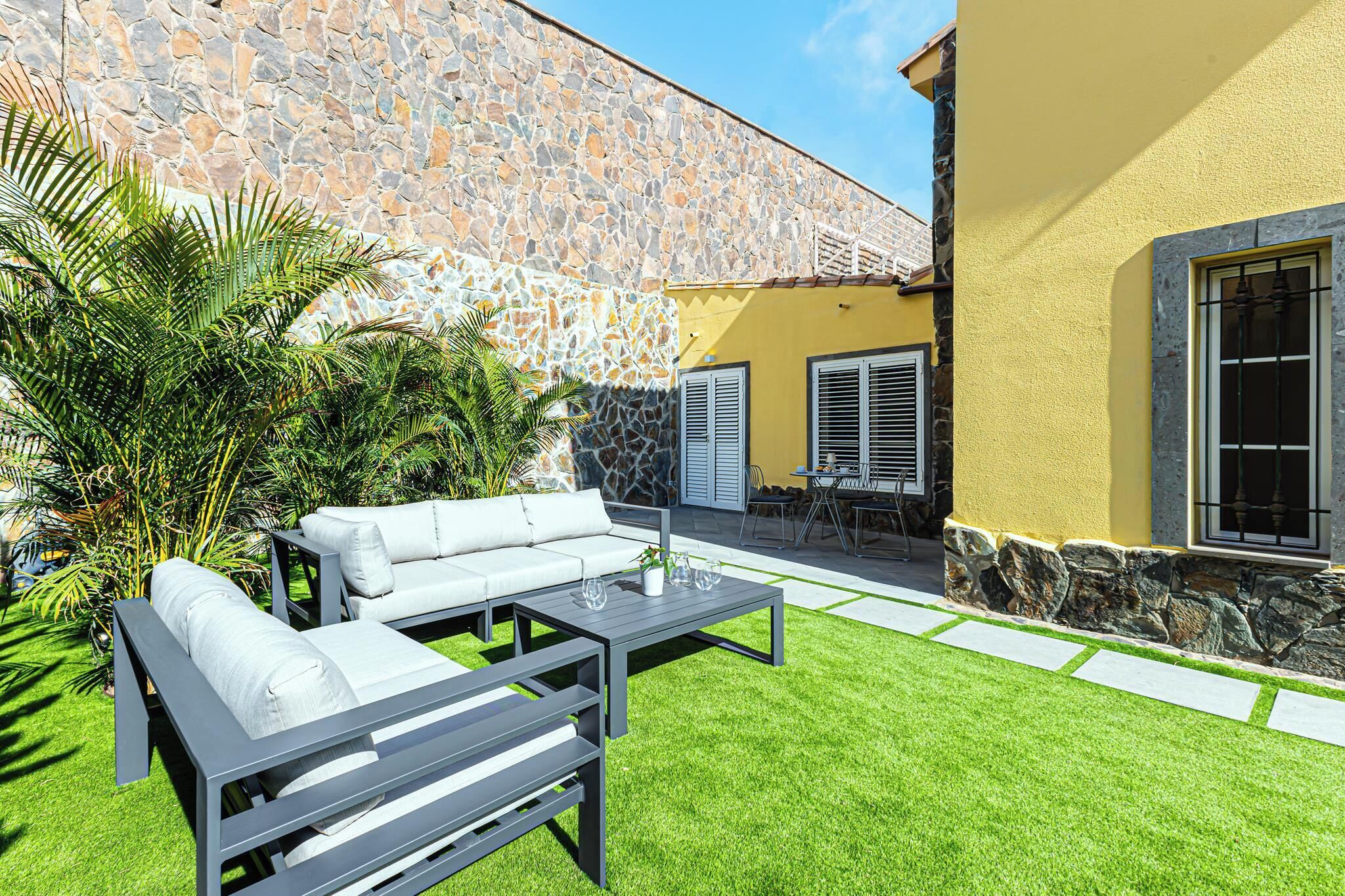 Un patio con pared de piedra, un edificio amarillo y mobiliario exterior.