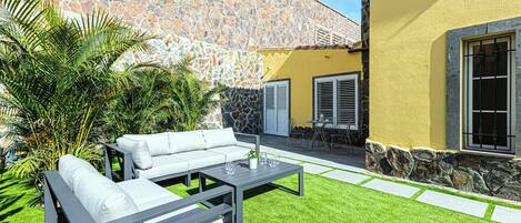 Un patio con pared de piedra, un edificio amarillo y mobiliario exterior.