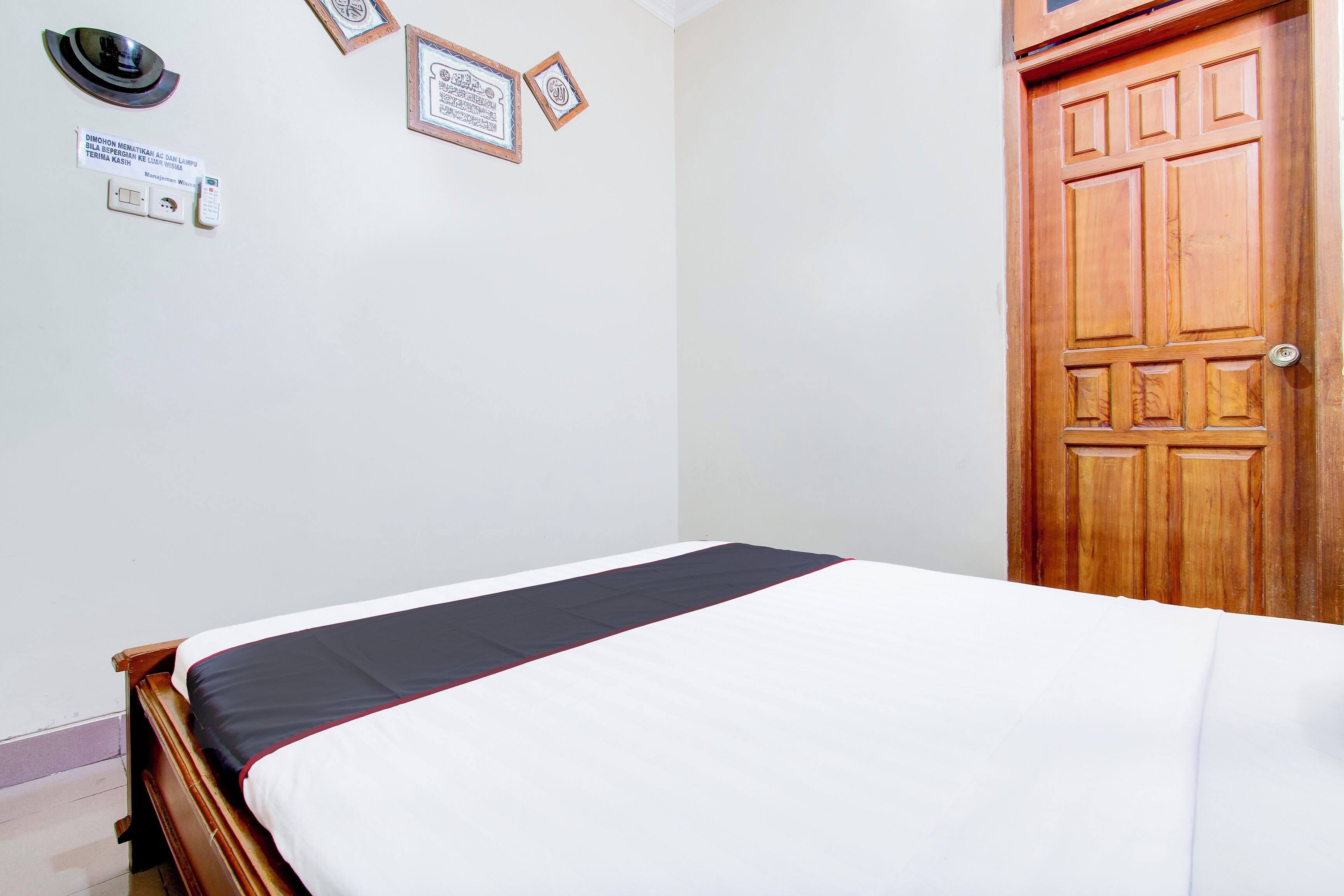 A neatly made bed with a white and dark-colored bedspread, a wooden door, and a wall with framed certificates.
