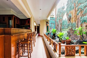 Corredor de hotel com bancos de bar de madeira, vista para uma parede rochosa com plantas e uma cascata.