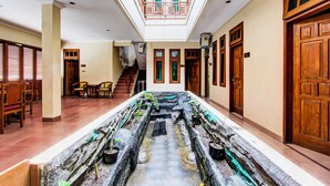 Eine Hotellobby mit einem zentralen Wasserspiel, Holztüren und einer Treppe, die in einen oberen Bereich führt.