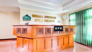 Ein Empfangstresen mit einem Schild, das 'Wisma Syariah Atma Bhakti' in verschiedenen Sprachen zeigt.