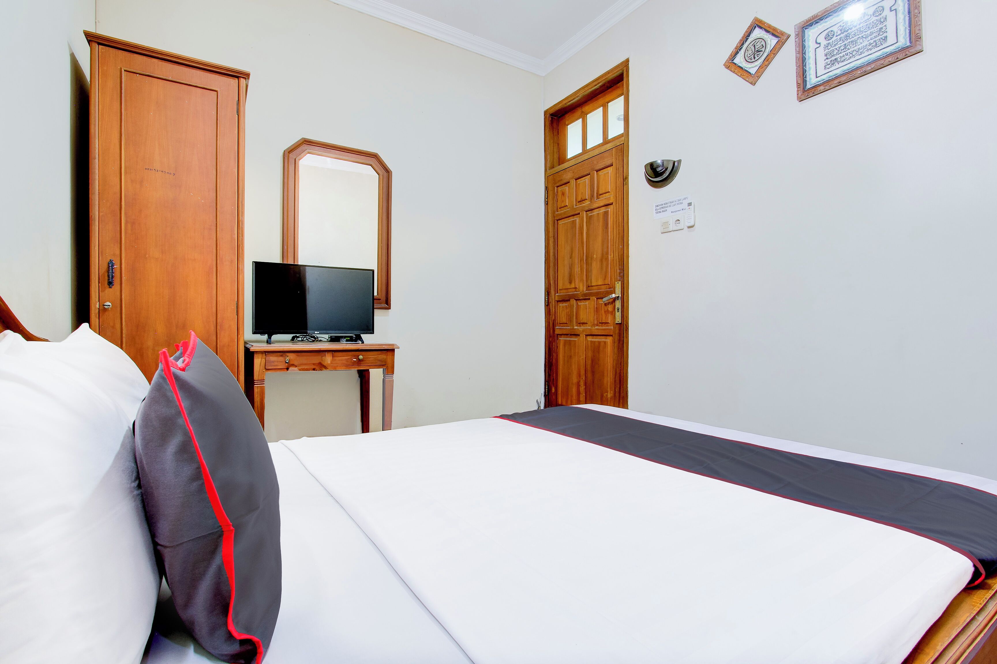 A hotel room with a bed, a television on a small table, a wardrobe, and a door.