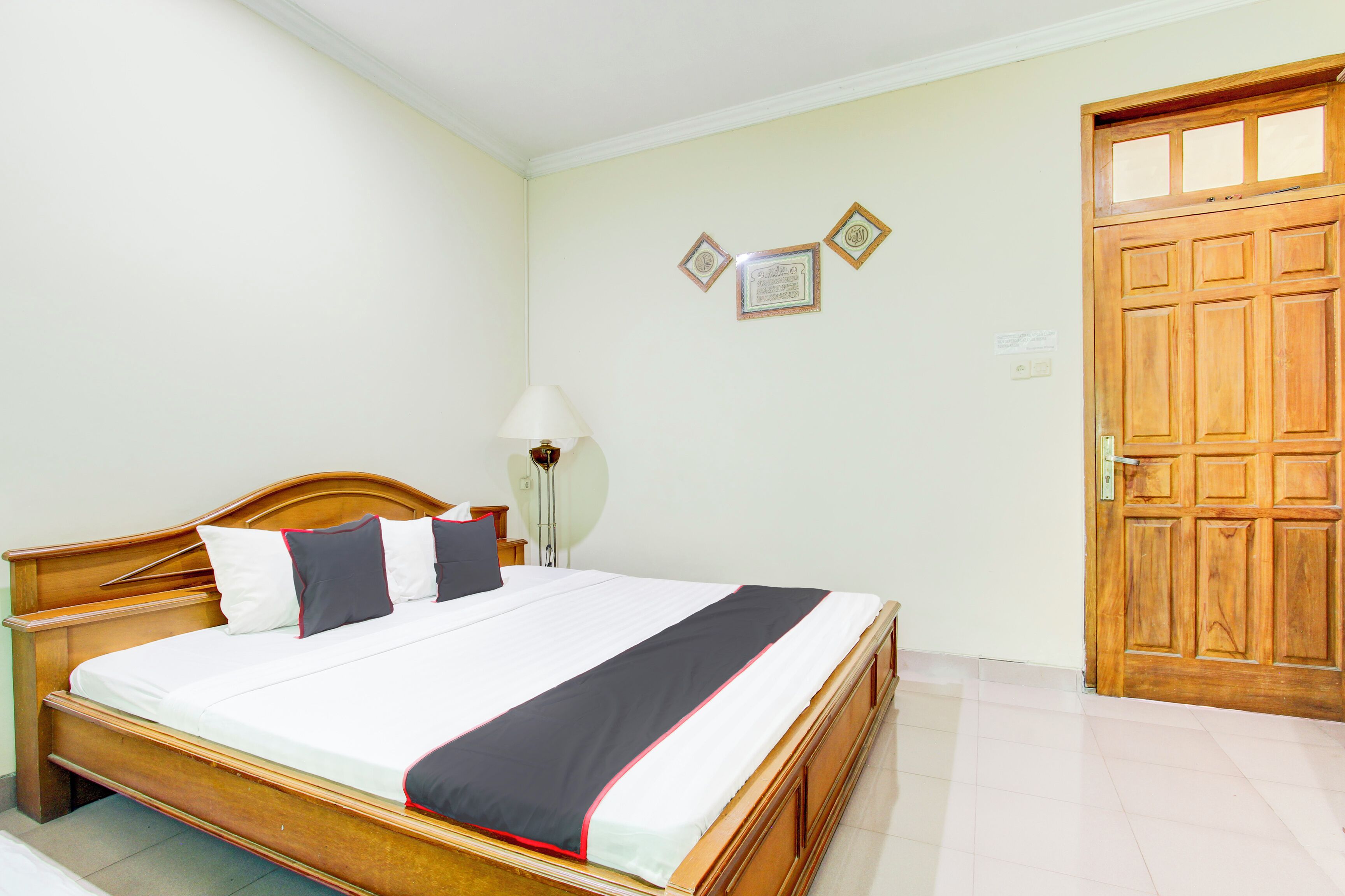 A neatly made bed with a wooden headboard, a bedside lamp, and a wooden door with glass panels.