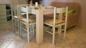 A dining area with a white table and chairs, a sofa with a green pillow, and a tiled floor. - Apartments Jukica (Vis)