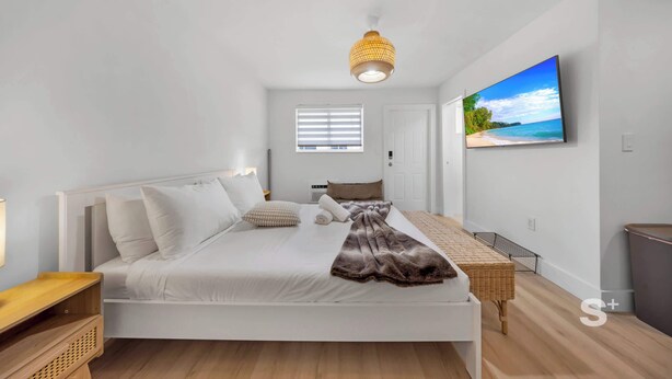 A modern bedroom with a bed, bedside table, and a TV on the wall. - Cozy Miami Studio | Free Parking | Gym | BBQ (Miami)