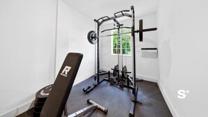 A compact gym with a bench, squat rack, and weight plates. - Cozy Miami Studio | Free Parking | Gym | BBQ (Miami)