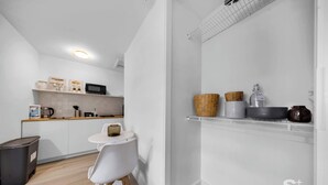 A modern kitchen with white cabinets, a microwave, and a small dining area with a white chair and table. - Cozy Miami Studio | Free Parking | Gym | BBQ (Miami)