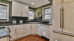 Una cocina con armarios blancos, encimera negra y refrigerador de acero inoxidable.