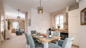 Une cuisine moderne avec des meubles blancs, une table à manger pour quatre personnes et un mur en pierre en arrière-plan.