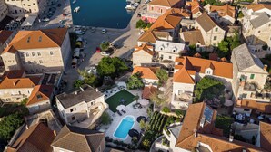Vue aérienne d’une ville côtière avec des bâtiments historiques, un port de plaisance et une piscine.